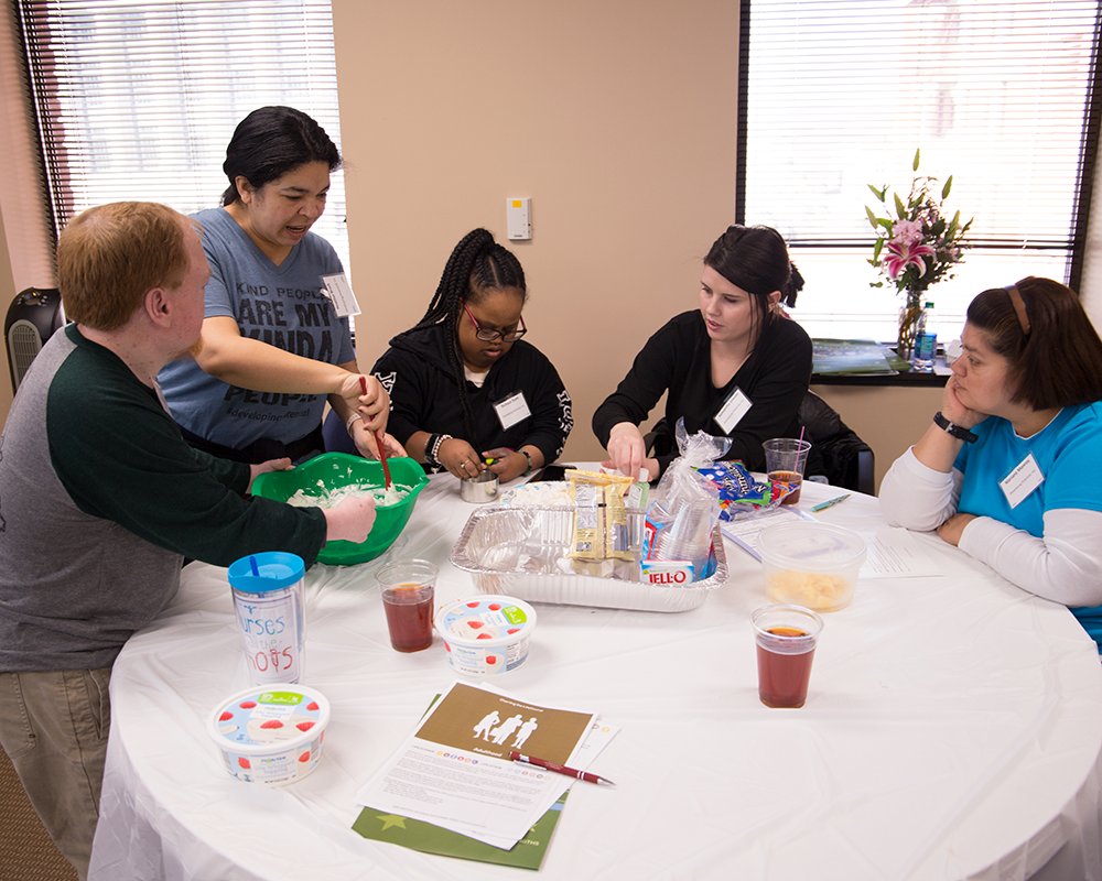 This photo shows attendees of the Charting the LifeCourse for Health (CtLC) event mixing together ingredients inside of a green bowl. They are preparing to make a tasty dessert!