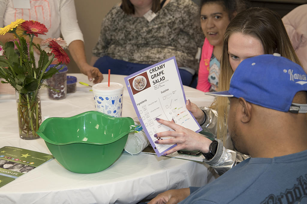 This photograph shows attendees of the Charting the LifeCourse for Health (CtLC) event reading instructions on how to create a creamy grape salad.