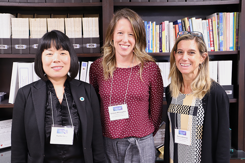 Three female attendees stand side-by-side in front of a bookshelf and pose for a photo.